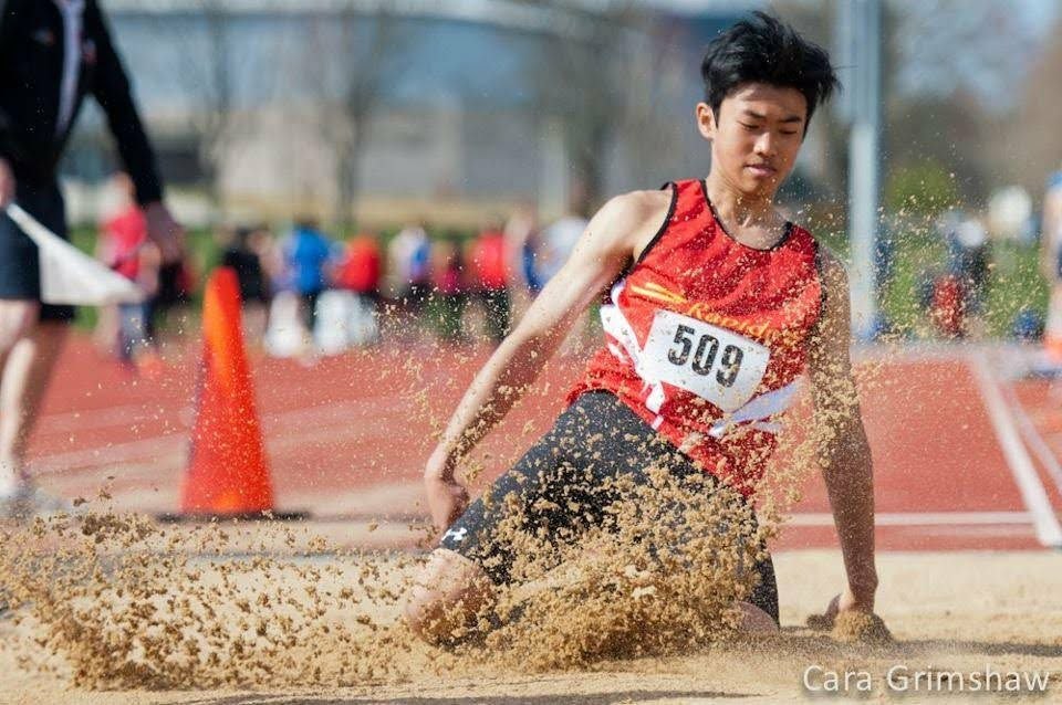 Club Rapide athlete mid-air during a long jump competition, wearing the club's red singlet
